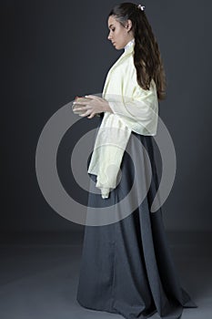 A Victorian or Edwardian woman standing and holding a pile of books