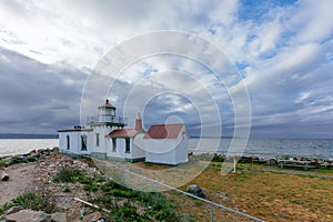 Victorian-era lighthouse under clouds by water in Discovery Park, Seattle, USA