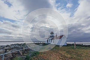 Victorian-era lighthouse under clouds by water in Discovery Park, Seattle, USA