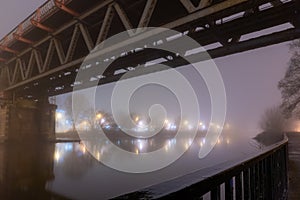 A Victorian steel railway bridge going over a river on a moody, atmospheric foggy winters night. Worcester, River Seven, UK