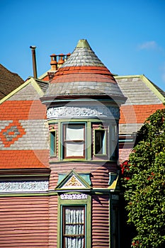 Victorian style spire or turret with red house pannels and decorative colors with front yard trees and visible chimney
