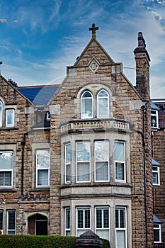 Victorian-style stone building with a gabled roof and bay windows under a blue sky with clouds, showcasing classic architectural