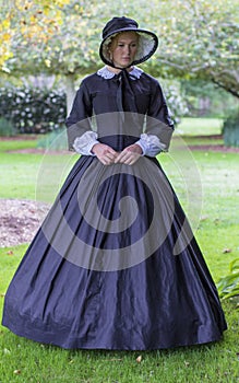 Victorian woman in black dress walks in a summer garden