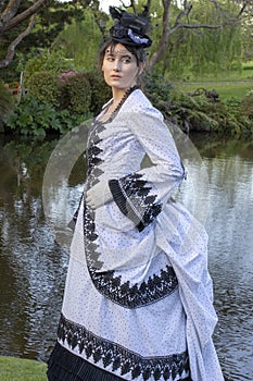 Victorian woman in black and white bustle dress standing in a garden