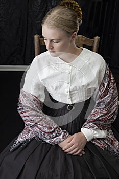 A Victorian woman with a tortoise shell comb in her hair is sitting in a chair.