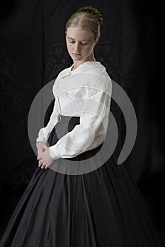 A Victorian woman with a tortoise shell comb in her hair stands against a dark backdrop.