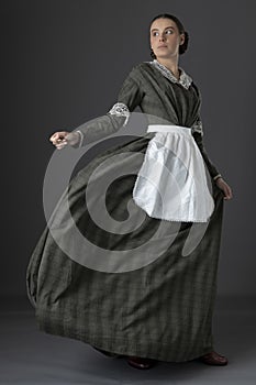 A working class Victorian woman wearing a dark green check bodice and skirt with an apron photo