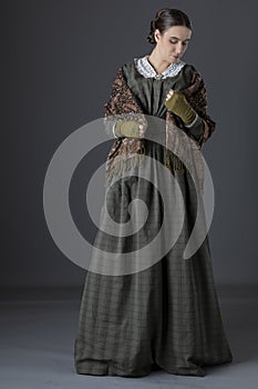 A working class Victorian woman wearing a dark green check bodice and skirt with an apron and holding a candle. photo