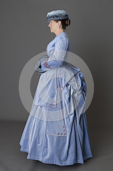 A Victorian woman wearing a pale blue velvet bustle ensemble with a fur muff and hat photo