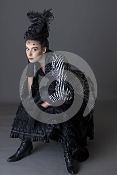 A Victorian woman wearing a striped silk polonaise and a black skirt and sitting down against a studio backdrop