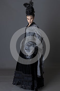 A Victorian woman wearing a striped silk polonaise and a black skirt and standing against a studio backdrop