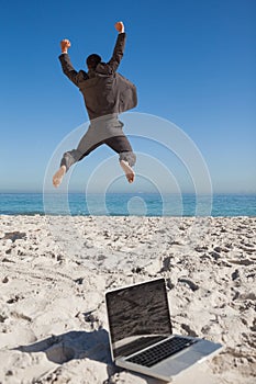 Victorious businessman in suit jumping leaving his laptop