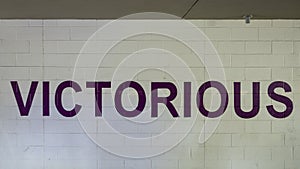 Victorious is painted in bold purple letters on a white brick wall in the parking garage on Victory Park Lane, Dallas, Texas