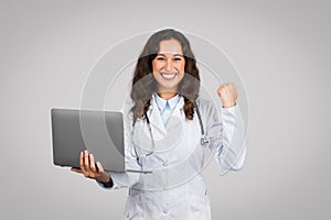 Victorious woman doctor with laptop celebrating success
