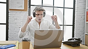 Victorious young caucasian man celebrating winning business success at office, exuding confidence with laptop and headphones
