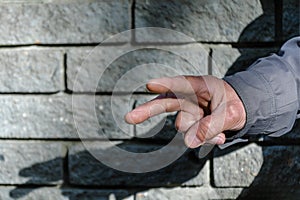 Victory hand sign. Gesture mens hand of two fingers. Concept of positive, peace, win. Closeup view on gray stone wall background.