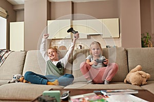 Victory. Little boy looking excited while playing video games with his sister, sitting on a couch in the living room