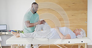 Video of african american male physiotherapist exercising with caucasian senior woman