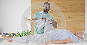 Video of african american male physiotherapist exercising with caucasian senior woman
