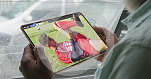 Video of african american man sitting on sofa and watching football on tablet at home