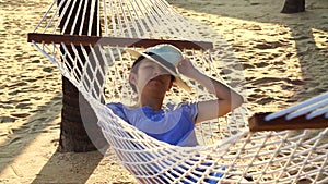 Video Asian woman, girl wearing hat relax on a hammock on the sunny beach with coconut trees