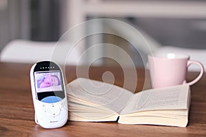 Video baby monitor with image of sleeping baby on the screen on the table with open book and tea mug. Mother relax time during chi