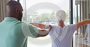 Video of back view of african american male physiotherapist exercising with caucasian senior woman