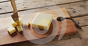 Video of block of cheese and knife in cubes of cheese on wooden board and rustic table