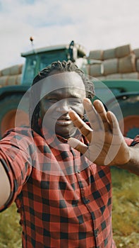 Video call. African farmer waving to the smartphone camere in front of the tractor