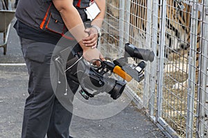 Video camera in the hands of a man close-up. The camera operator works with his equipment. Concept: reportage shooting, news, work