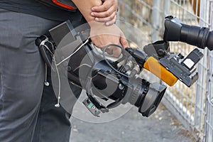 Video camera in the hands of a man close-up. The camera operator works with his equipment. Concept: reportage shooting, news, work