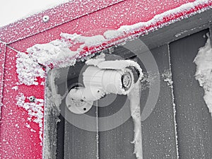 Video camera on the home wall in winter. Icicles on the camera block the lens. Frozen security camera in winter with ice crystals