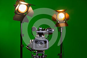 A video camera and a spotlight with a Fresnel lens on a green background. Filming in the interior. The chroma key