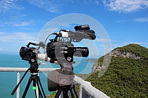 Video camera on a tripod on top of the mountain. Ocean and blue