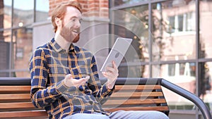 Video Chat on Tablet by Redhead Beard Young Man Sitting on Bench
