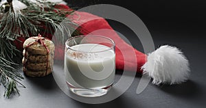 Video of christma cookies, glass of miljk, santa clasus hat and copy space on black background