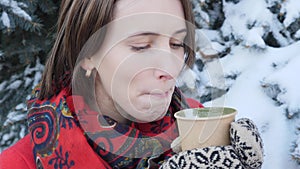 This video is about Close-up of the face of a girl who drinks hot tea or coffee in the winter on the street, she wears knitted mit