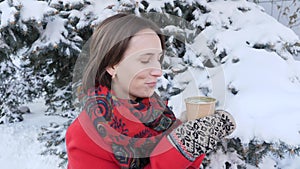 This video is about Close-up of the face of a girl who drinks hot tea or coffee in the winter on the street, she wears knitted mit