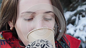 This video is about Close-up of the face of a girl who drinks hot tea or coffee in the winter on the street, she wears knitted mit