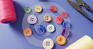 Video of colourful buttons with thread snippers and reels of cotton on blue background