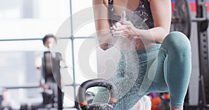 Video of confident caucasian woman powdering hands before working out with kettlebell weight at gym