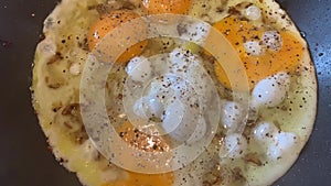 Video of cooking of fried eggs from several eggs with onions and black pepper, liquid egg white, a teflon frying pan