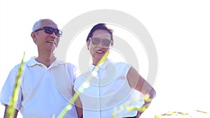 Video Cool Asian senior couple enjoying sunshine in nature wearing sunglasses and white shirts