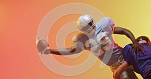 Video of diverse american football players tackling with ball over yellow to orange background