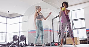 Video of diverse female fitness trainer instructing woman doing squats with kettlebell weight at gym