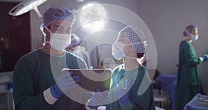 Video of diverse male and female surgeon in discussion, looking at tablet in operating theatre