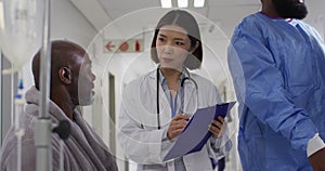 Video of diverse male patient and female doctor writing notes talking in busy hospital corridor