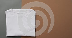 Video of flat lay of folded white t shirt with copy space on grey and brown background