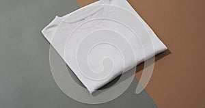 Video of flat lay of folded white t shirt with copy space on grey and brown background