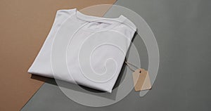 Video of flat lay of folded white t shirt with tag and copy space on grey and brown background